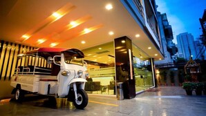A modern building with a well-lit entrance, a parked tuk-tuk, and a view of the cityscape in the background. - iCheck inn Residences Sukhumvit 20 (Bangkok)