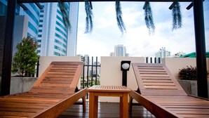 A rooftop lounge area with wooden loungers and a table, overlooking a cityscape with modern buildings. - iCheck inn Residences Sukhumvit 20 (Bangkok)