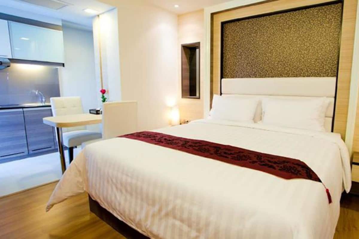 A modern hotel room with a large bed, a desk, and a kitchenette.