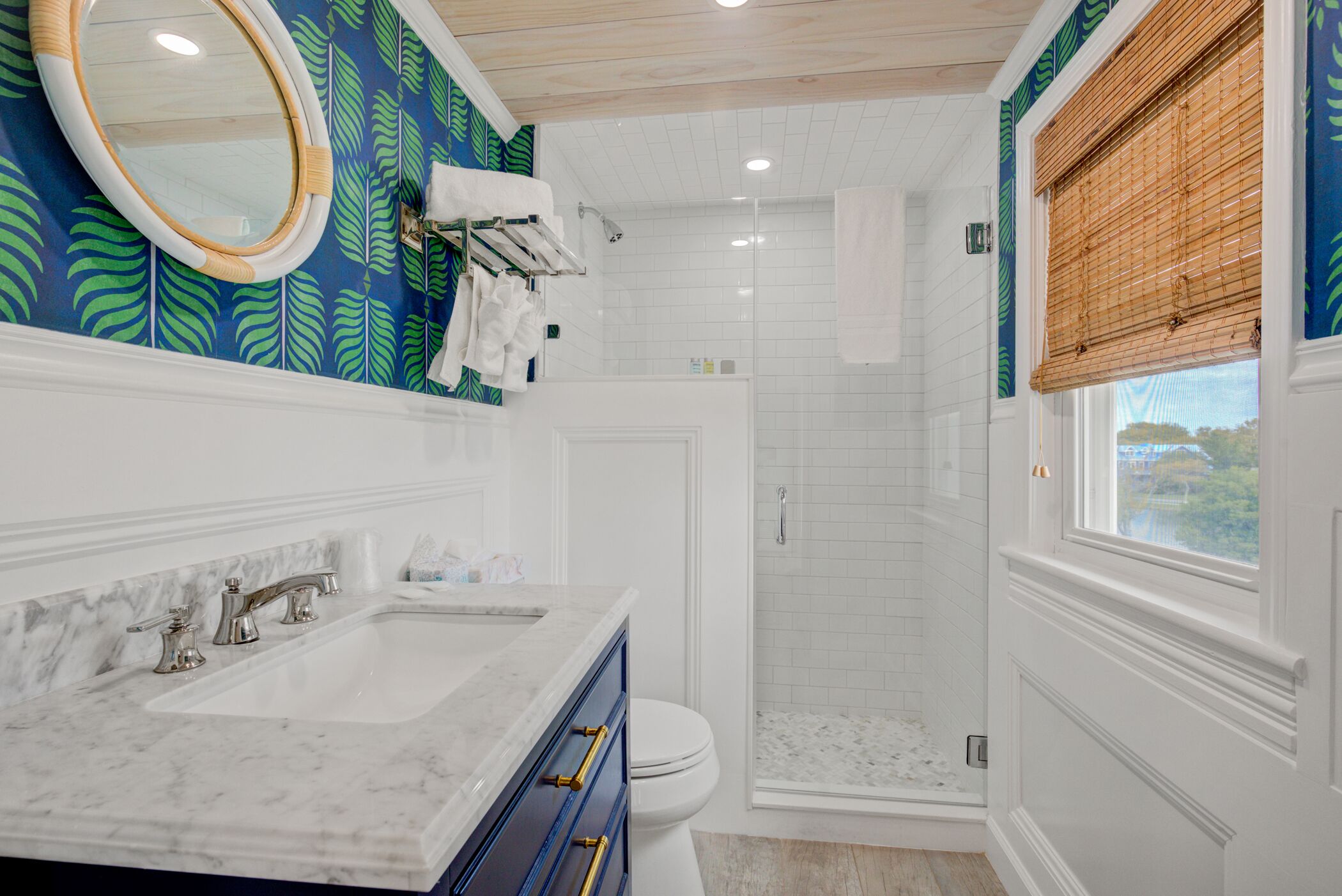 A bathroom with a white vanity, a large mirror, a shower with a glass door, and a window with a view.