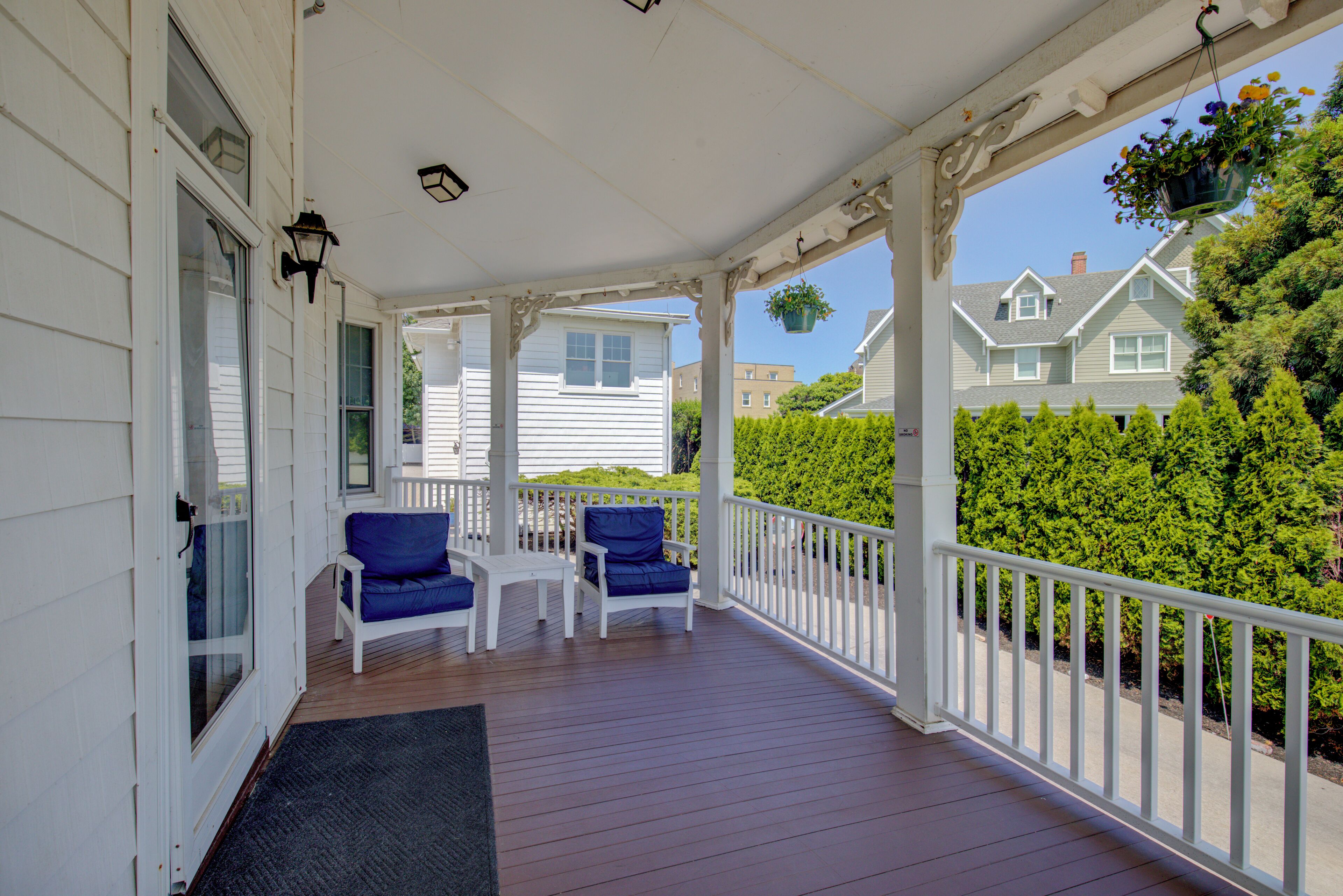 Een overdekte veranda met twee blauwe stoelen, een witte balustrade en uitzicht op omliggende huizen.