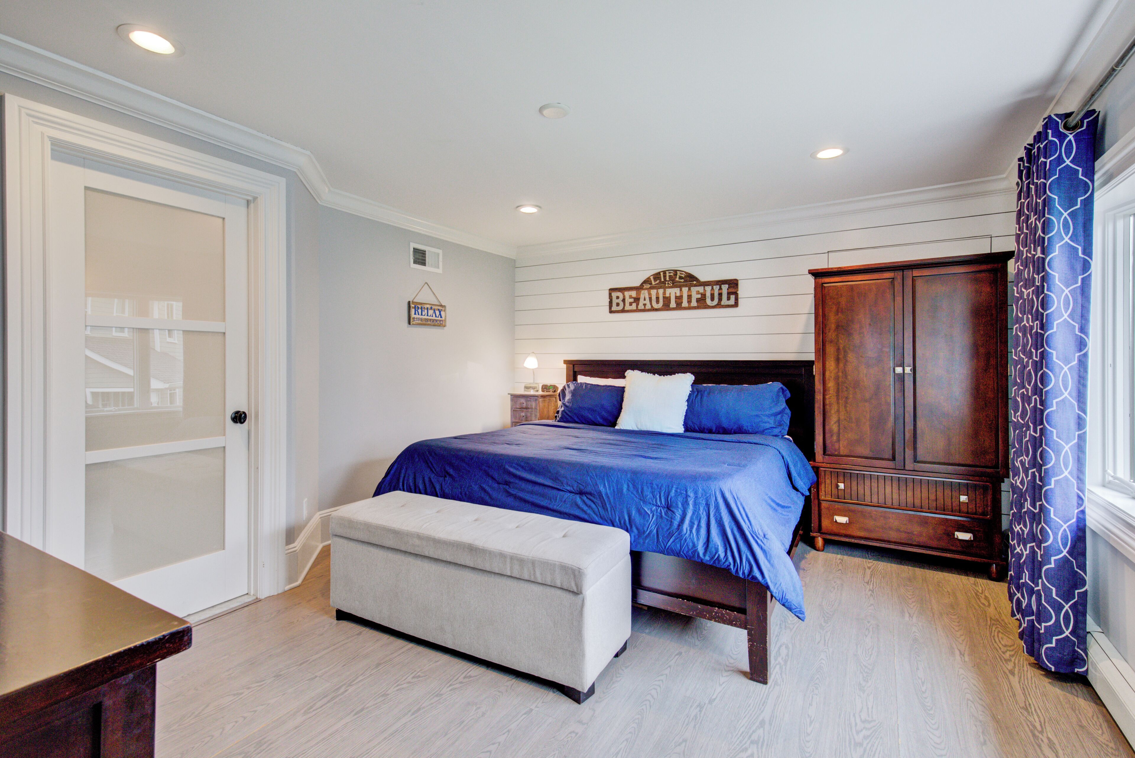A bedroom with a bed, a wooden wardrobe, a bench, and a door.