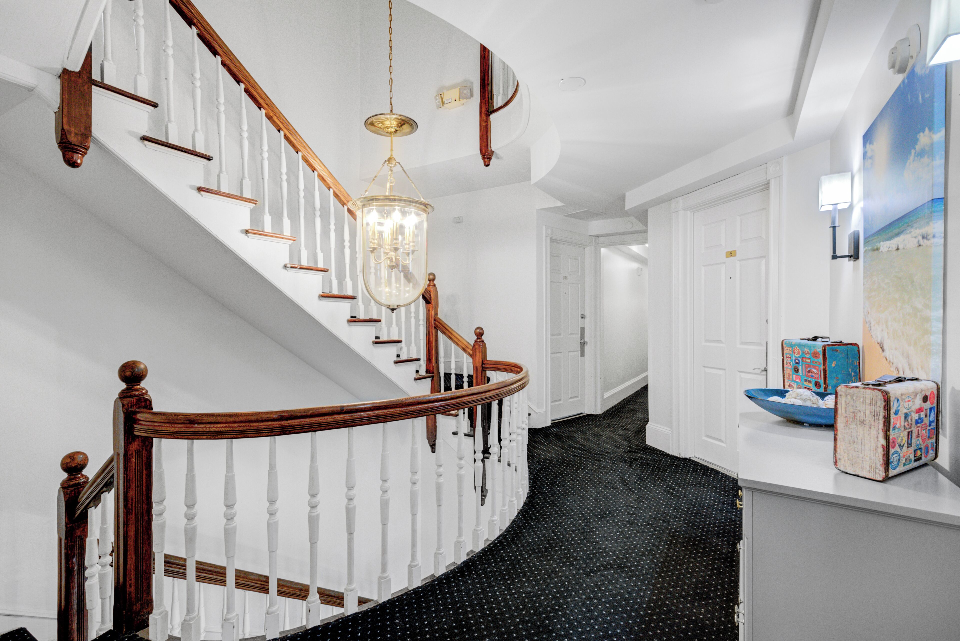A staircase with white balusters and wooden handrails, a chandelier, and a black polka dot floor.