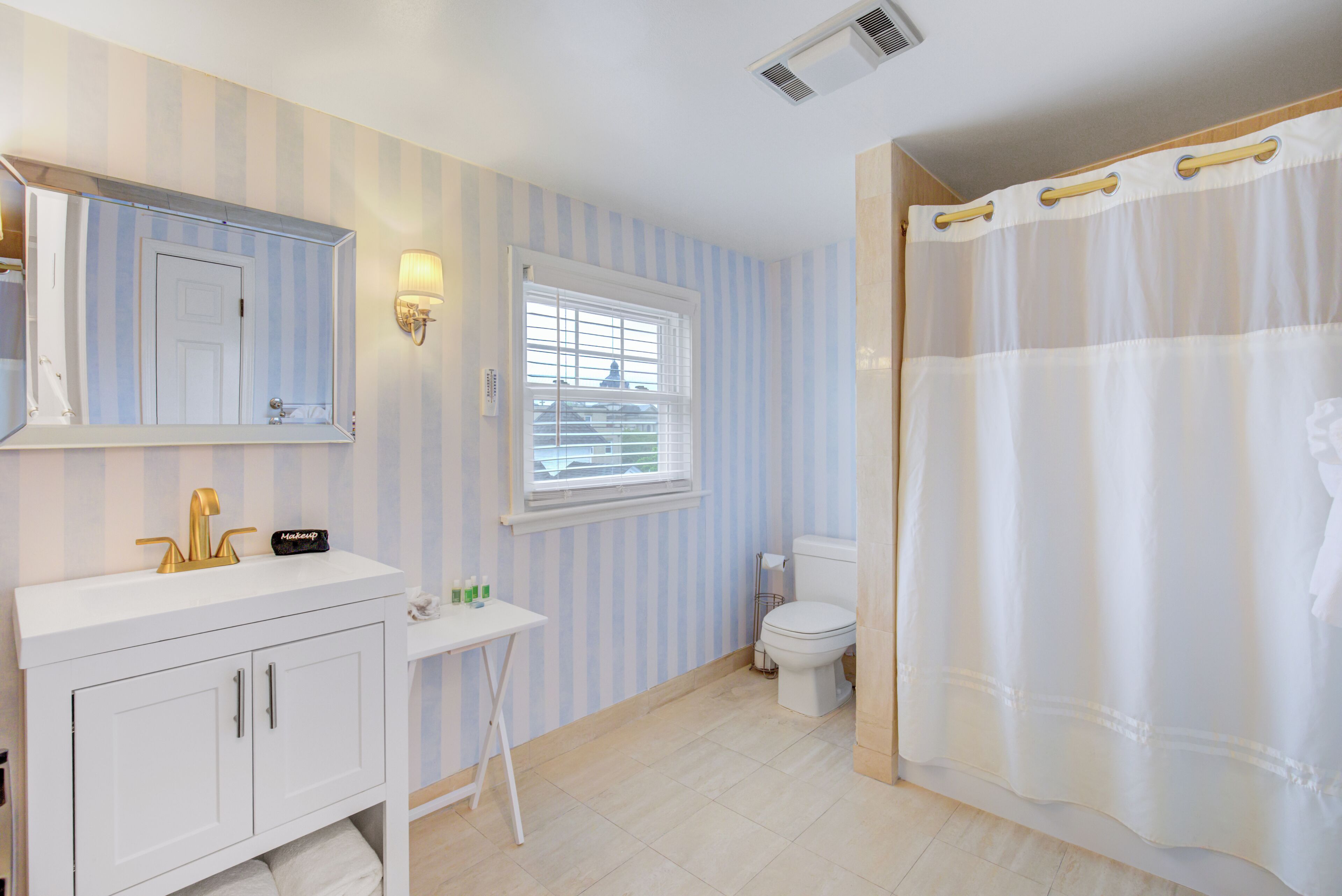 A bathroom with a white vanity, a mirror, a window, a toilet, and a shower curtain.