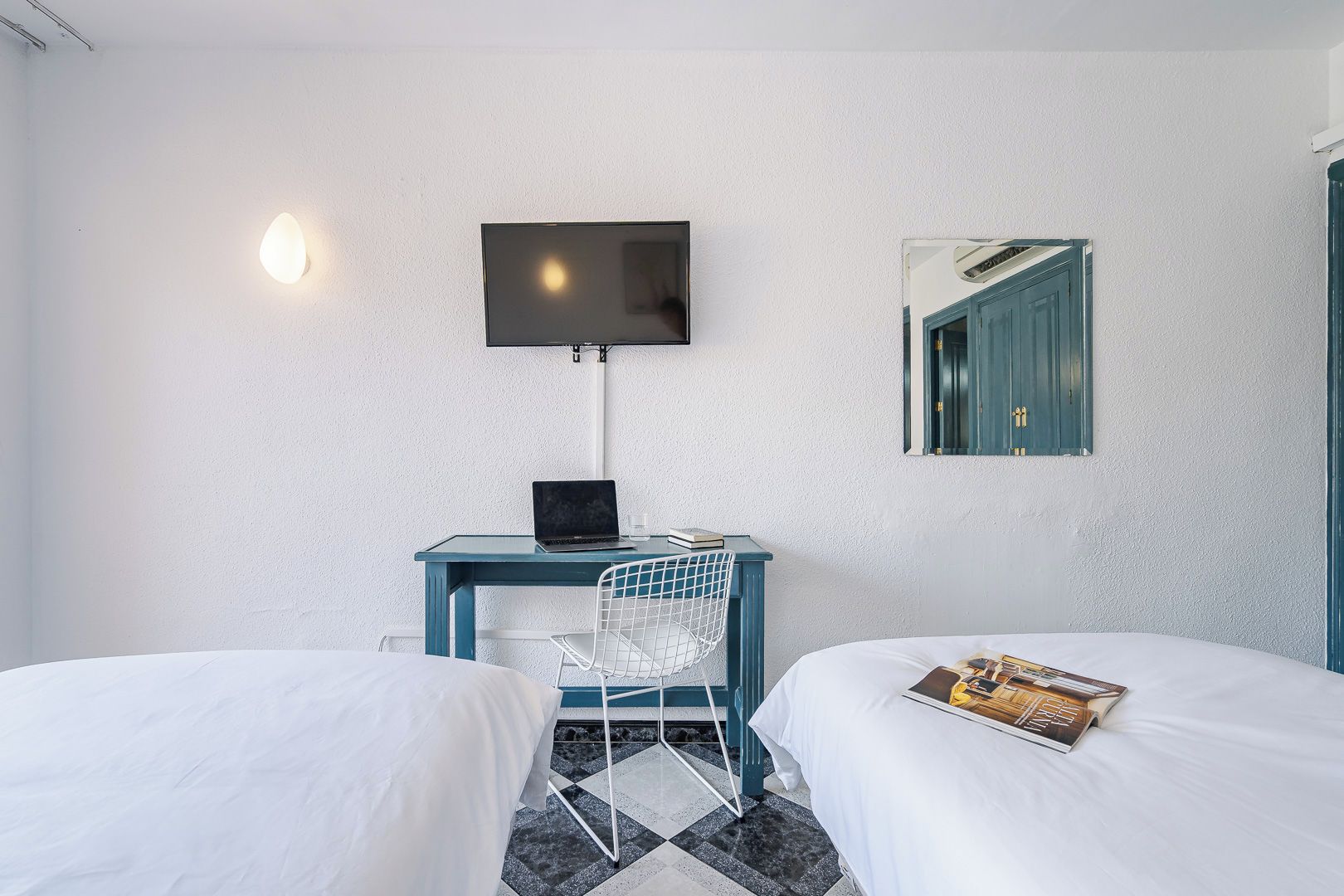 A hotel room with two beds, a desk with a laptop, a chair, a TV mounted on the wall, and a framed picture.