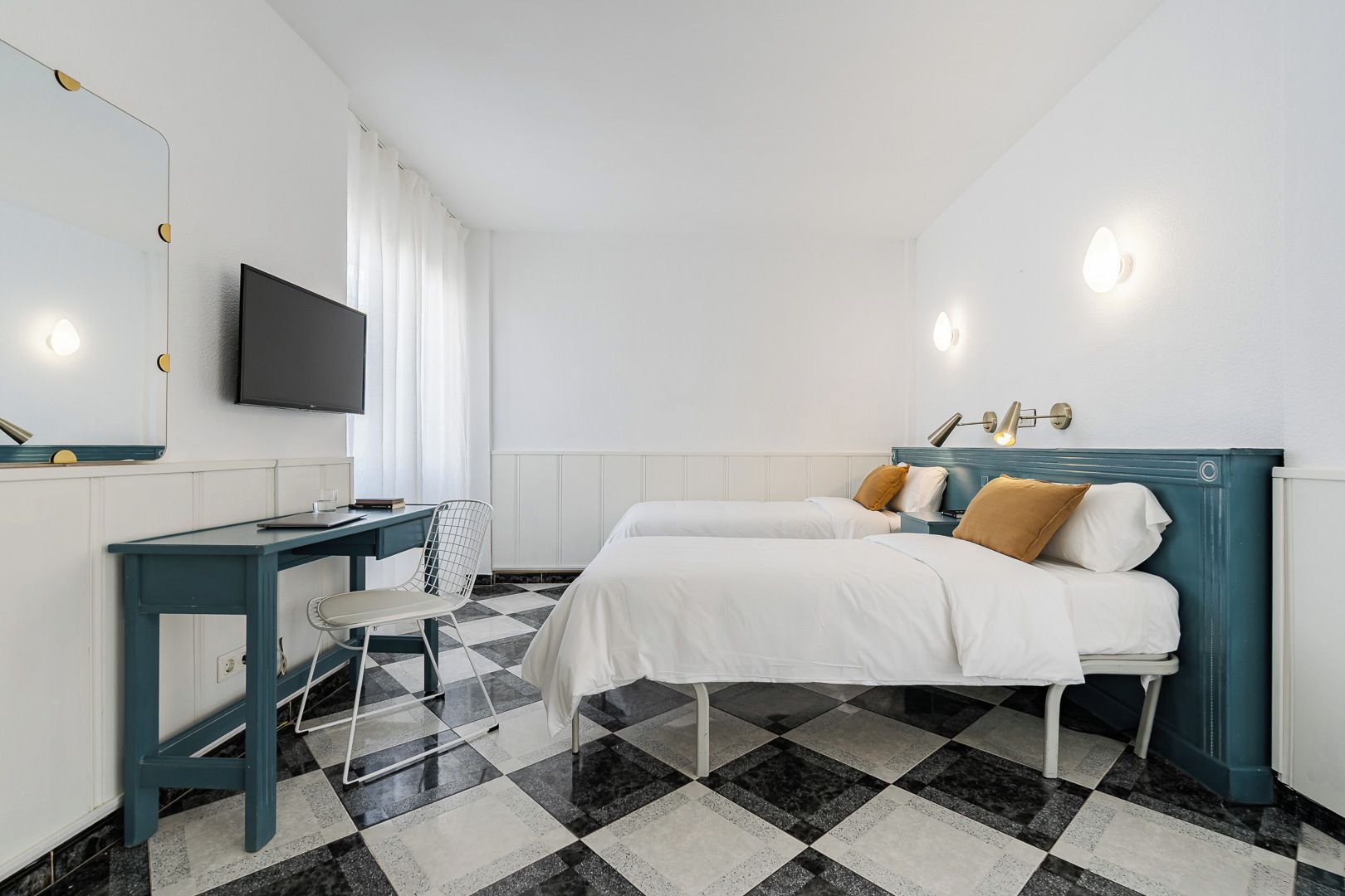 A hotel room with a bed, a desk, a chair, a television, and a checkered floor.