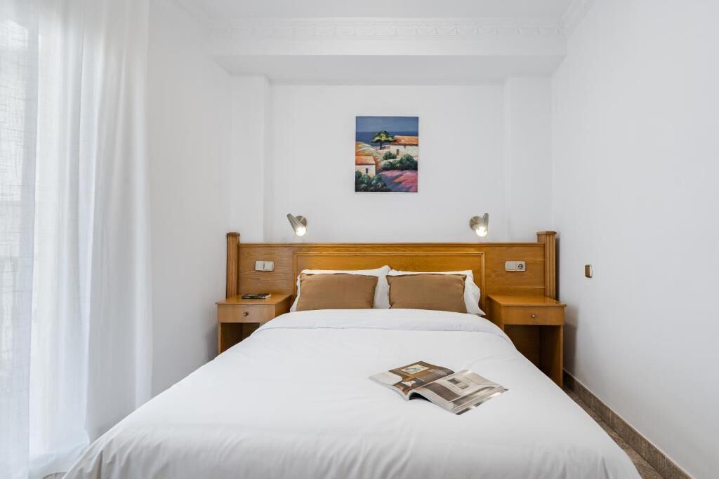 A hotel room with a large bed, wooden headboard, two bedside tables, and a painting on the wall.