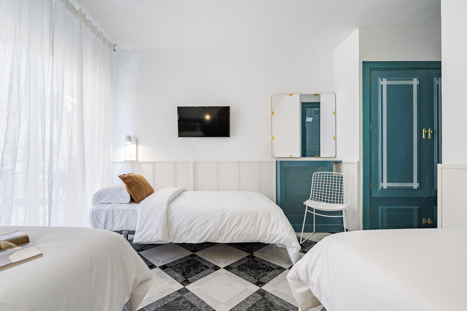 A hotel room with two beds, a TV, a mirror, a chair, and a teal door.