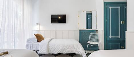 A hotel room with two beds, a TV, a mirror, a chair, and a teal door.