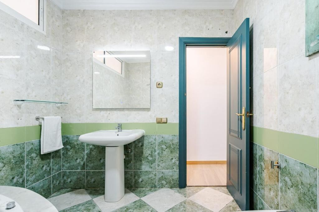 A bathroom with a sink, mirror, and green-tiled walls.