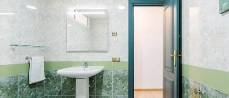 A bathroom with a sink, mirror, and green-tiled walls.