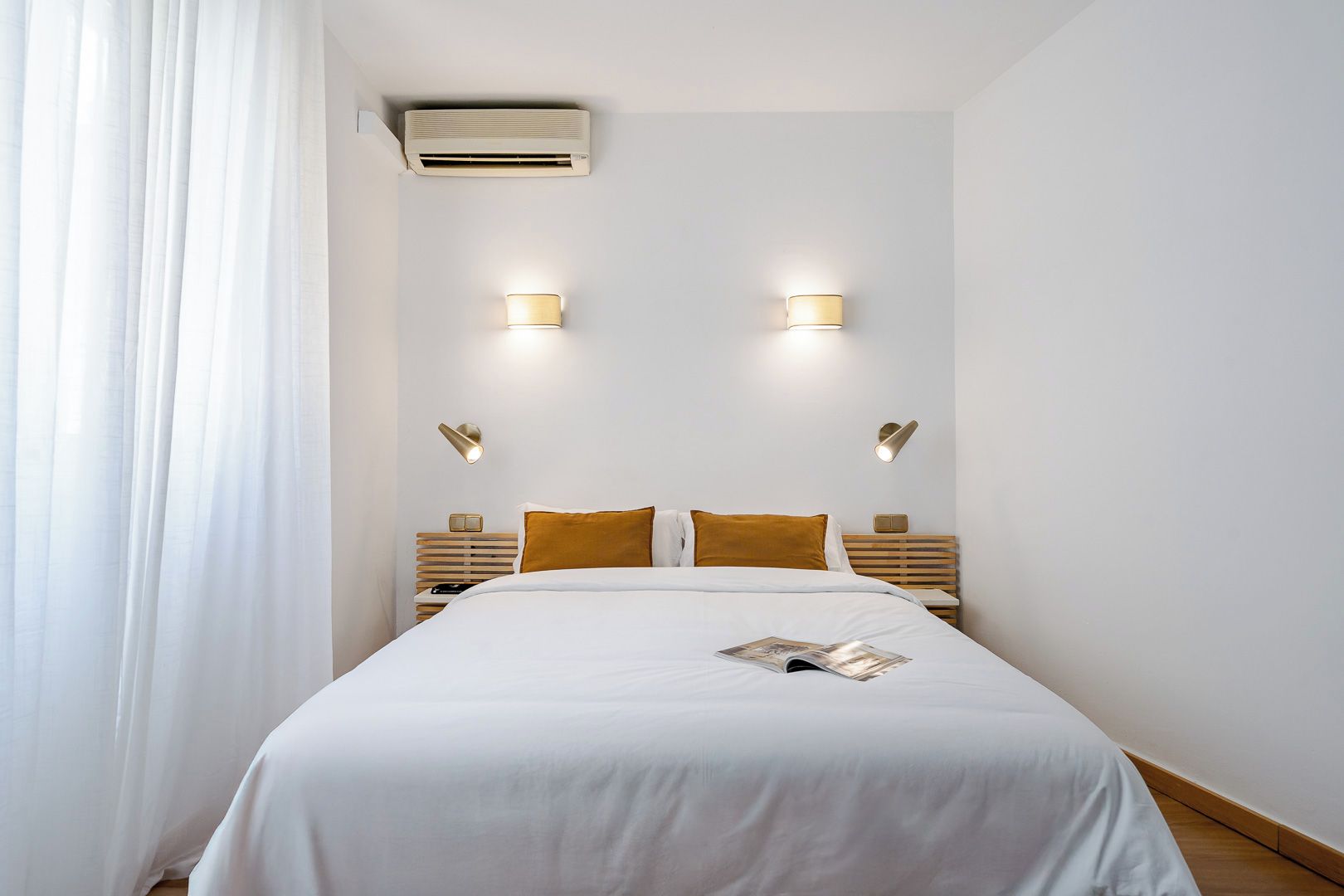 Ein Hotelzimmer mit einem Bett, zwei Nachttischen, einer Wandklimaanlage und zwei Wandleuchten.