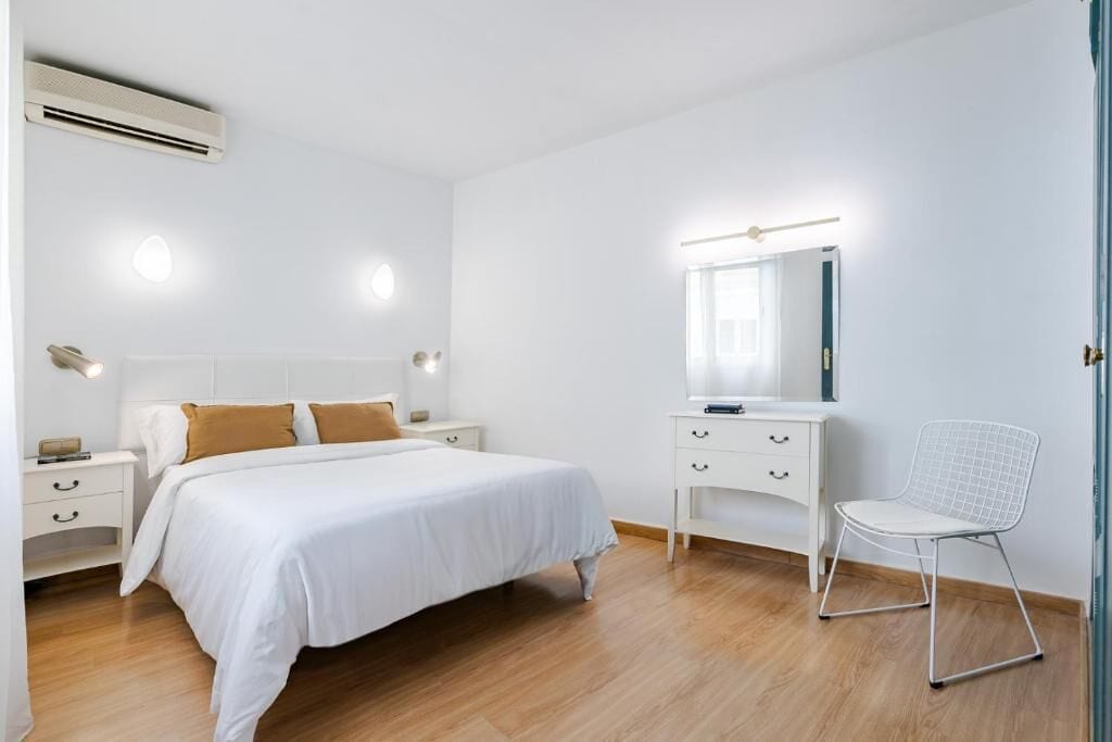 Un dormitorio con cama, mesitas de noche, cómoda, silla y espejo.