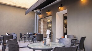 An outdoor patio area with round tables and chairs, a brick wall, and a modern light fixture. - Hotel Agur (Fuengirola)