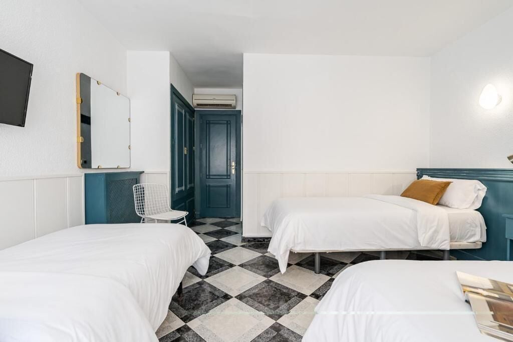A room with two beds, a chair, a mirror, and a door leading to another room.