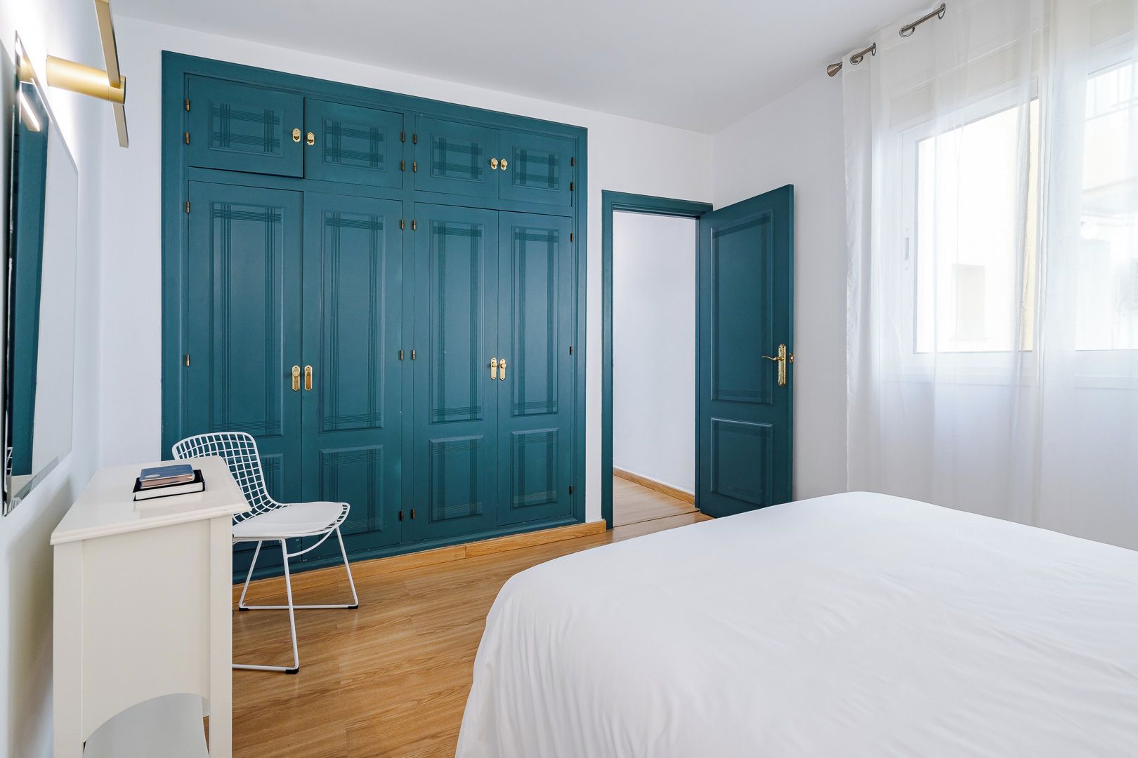 Une chambre à coucher avec un lit, un bureau blanc, une chaise et une grande armoire bleue.