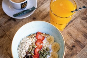 Un tazón de avena con frutas y nueces, una taza de café y un vaso de jugo de naranja sobre una mesa de madera.