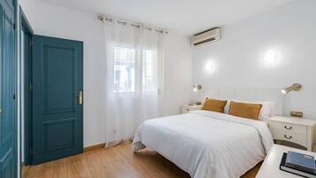 Un dormitorio con cama, mesitas de noche, cortinas en la ventana y un equipo de aire acondicionado.