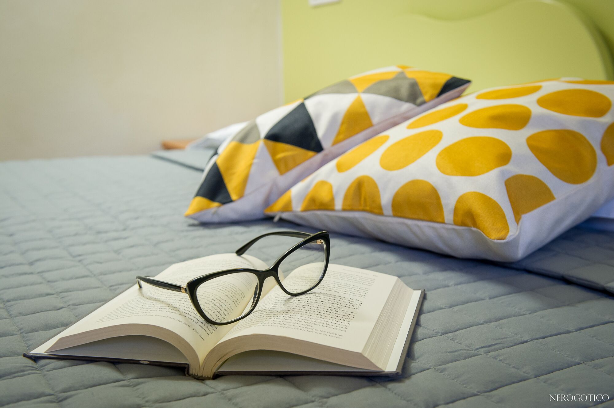 Un libro abierto con gafas encima, sobre una cama con cubierta acolchada.