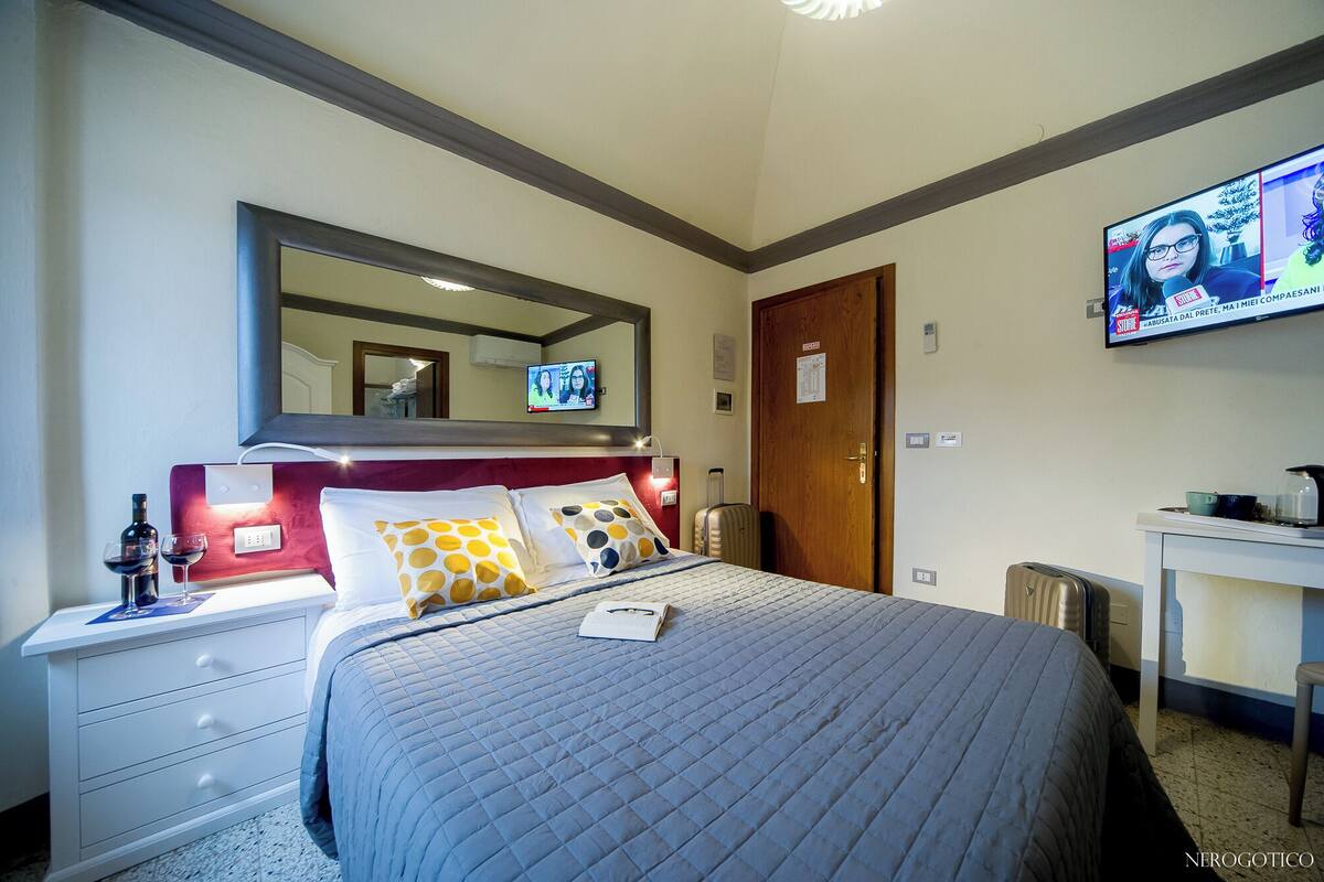 Ett hotellrum med en säng, ett skrivbord, en tv och en spegel.