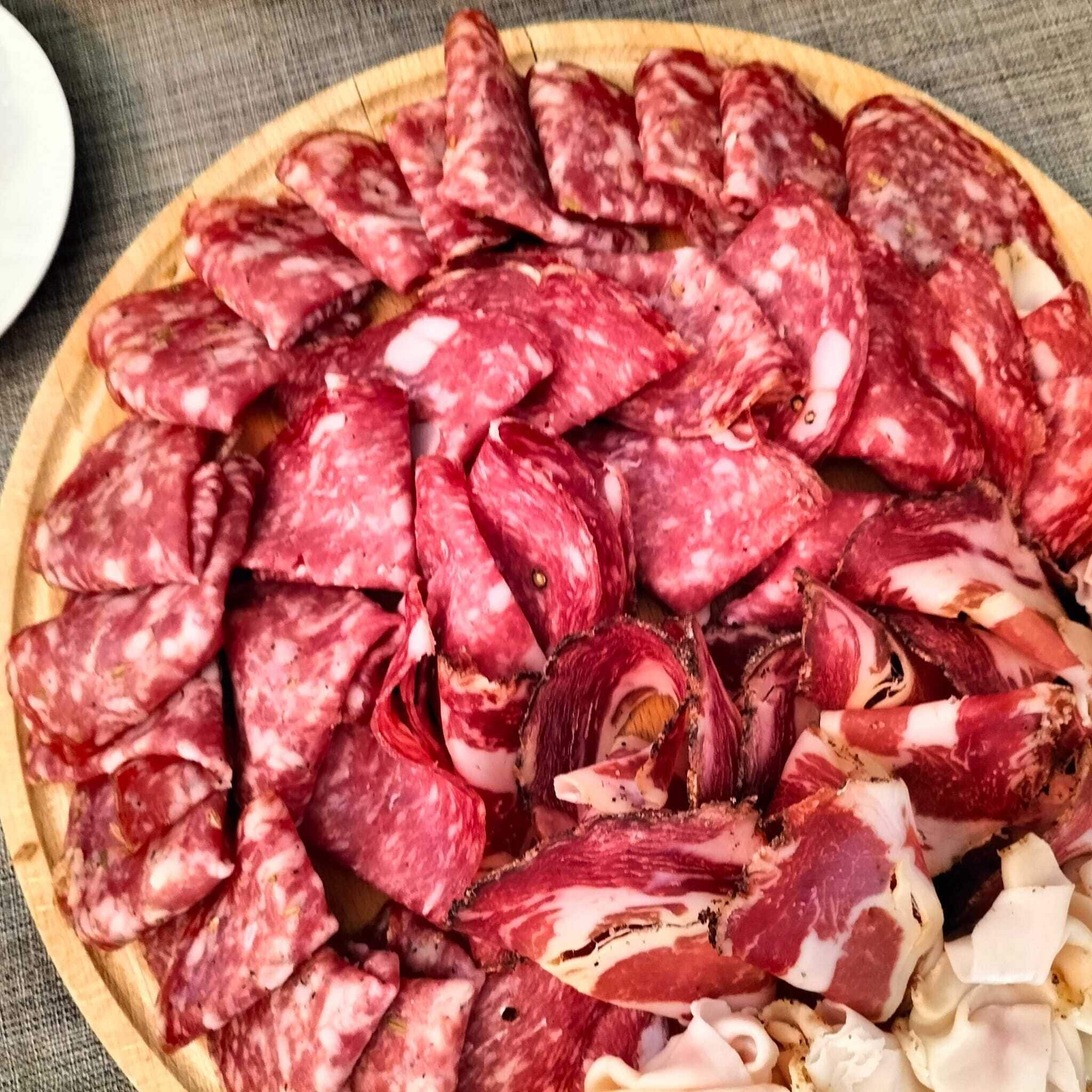 Uma tábua de madeira redonda com diversos tipos de charcutaria fatiada.