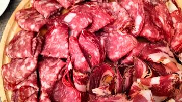 Uma tábua de madeira redonda com diversos tipos de charcutaria fatiada.