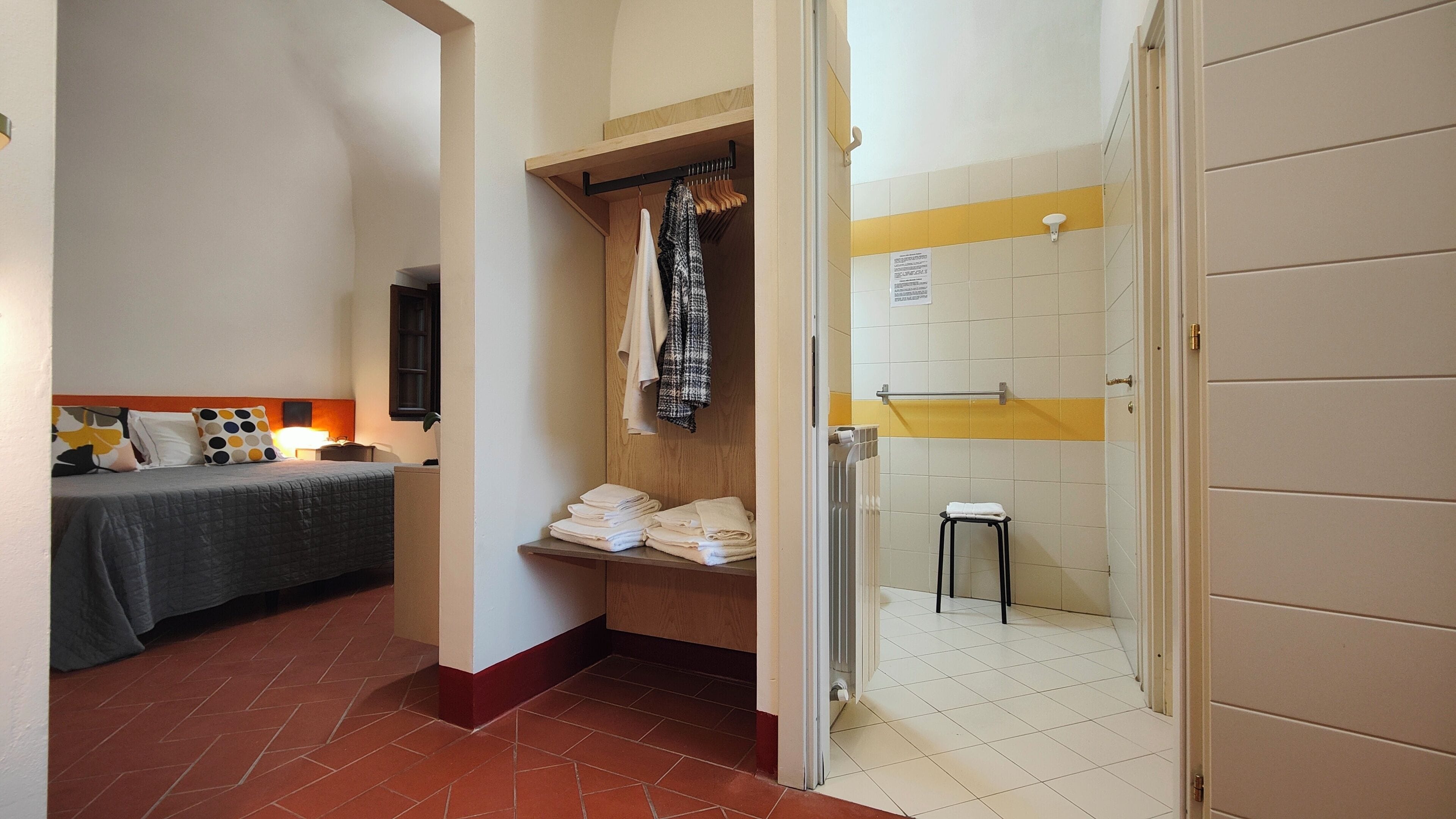Ein Hotelzimmer mit einem Bett, einem Holzschrank, einem kleinen Hocker und einer Duschkabine.