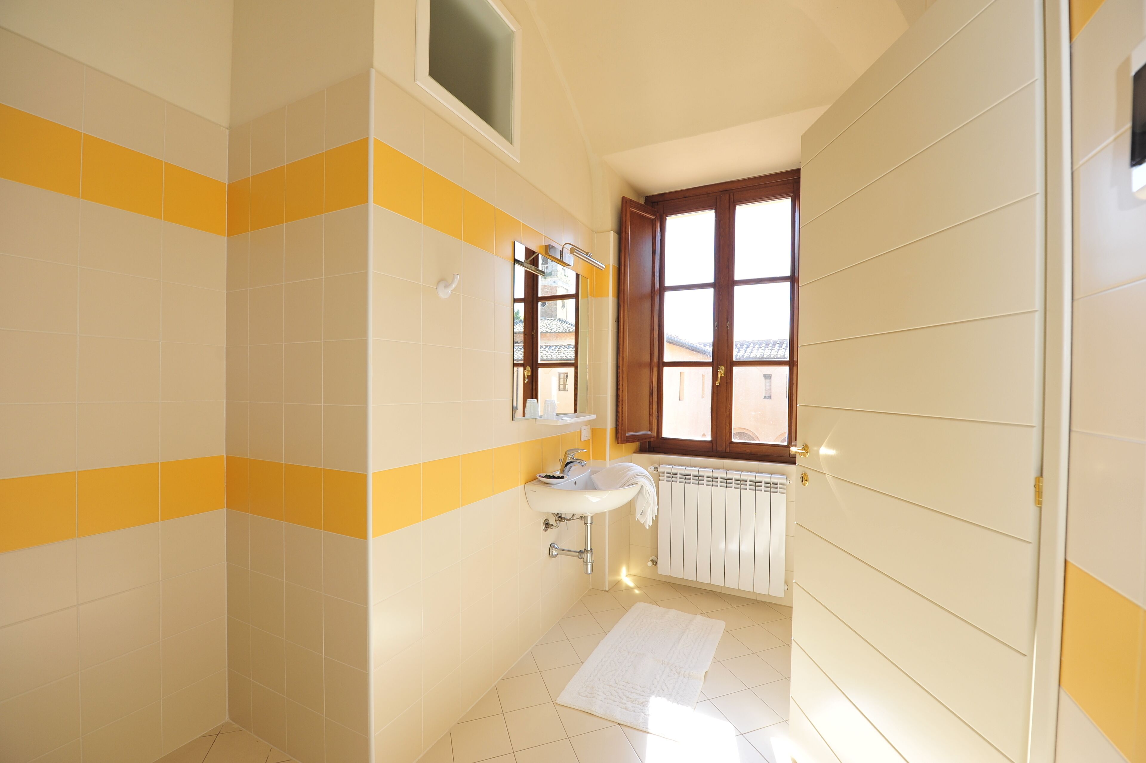Un baño con azulejos amarillos y blancos, un lavamanos, un espejo y una ventana.