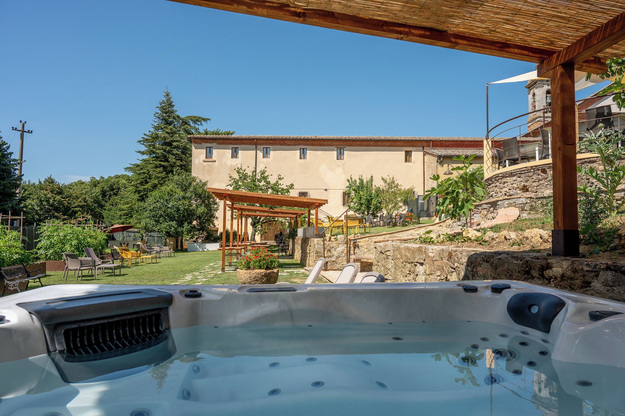 A hot tub in a backyard with a pergola, outdoor seating, and a stone wall.