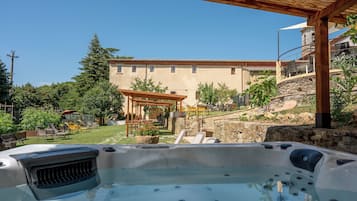 A hot tub in a backyard with a pergola, outdoor seating, and a stone wall.