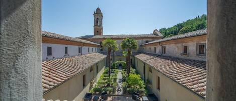 Un patio con un sendero central, rodeado de edificios con tejados de terracota y una torre del reloj al fondo.
