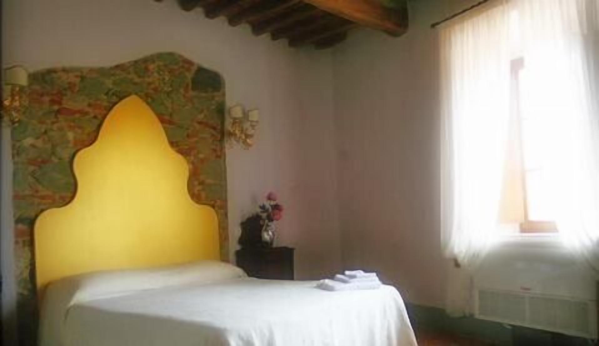 A bedroom with a bed, a nightstand, a wall-mounted lamp, and a window with curtains.