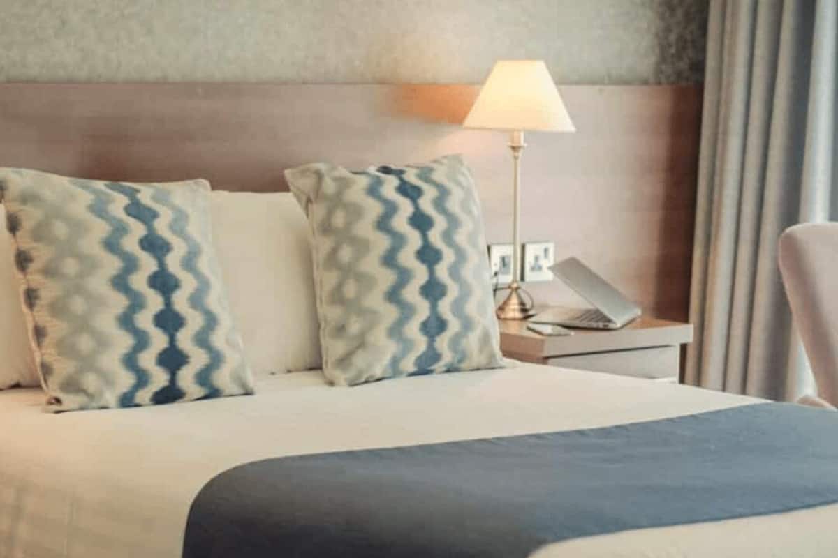 Ein Hotelzimmer mit Bett, Kissen, Nachttisch, Lampe und Stuhl.
