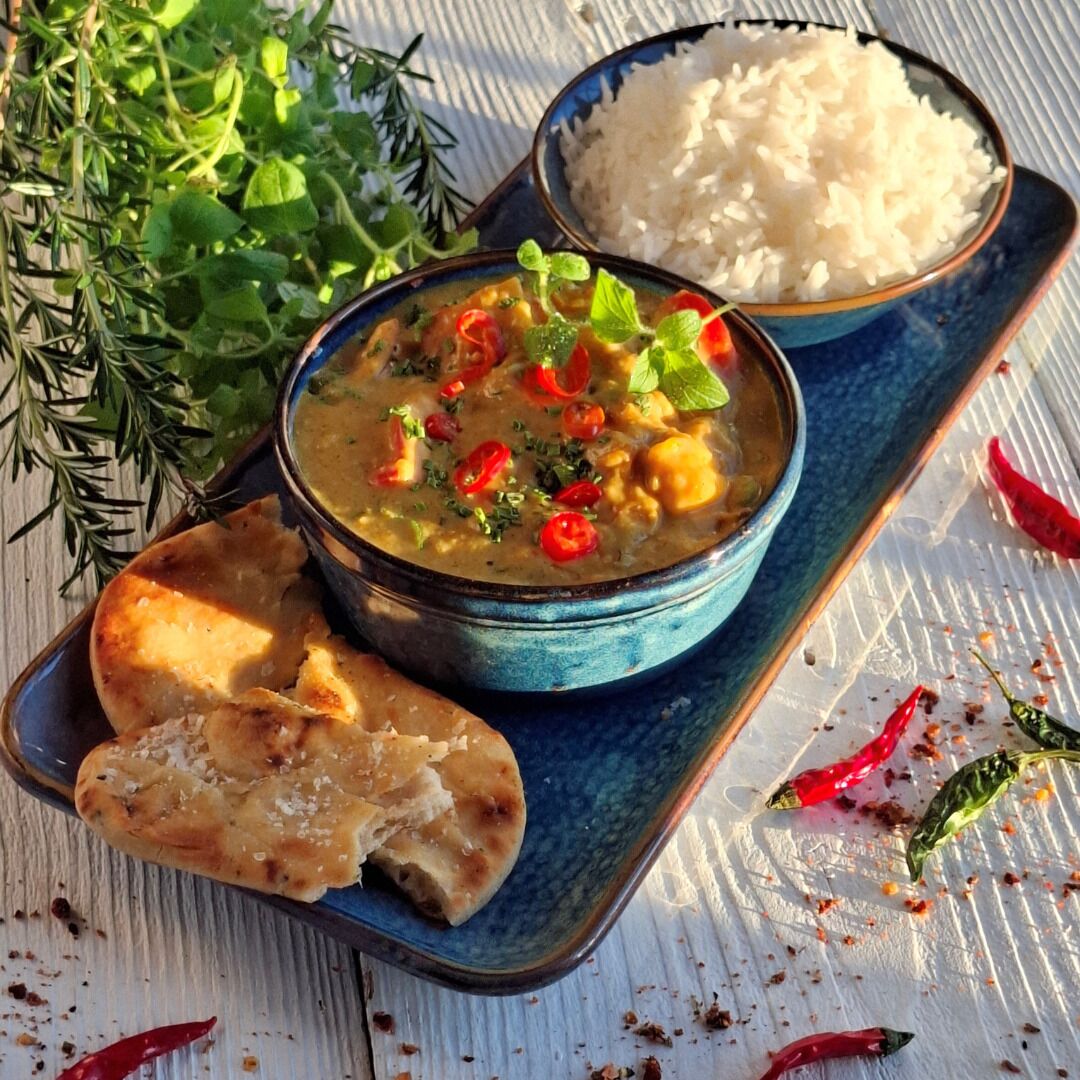 A bowl of curry with rice and naan bread on a wooden table.