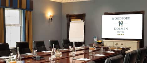 A conference room with a long table, black chairs, a projector screen, and a whiteboard.