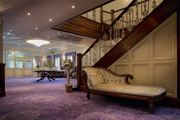 Una sala elegante con una gran escalera, un sofá lujoso y una mesa con un florero.