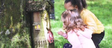 Dos niños interactúan con una casa de pájaros de madera sujeta a un árbol.