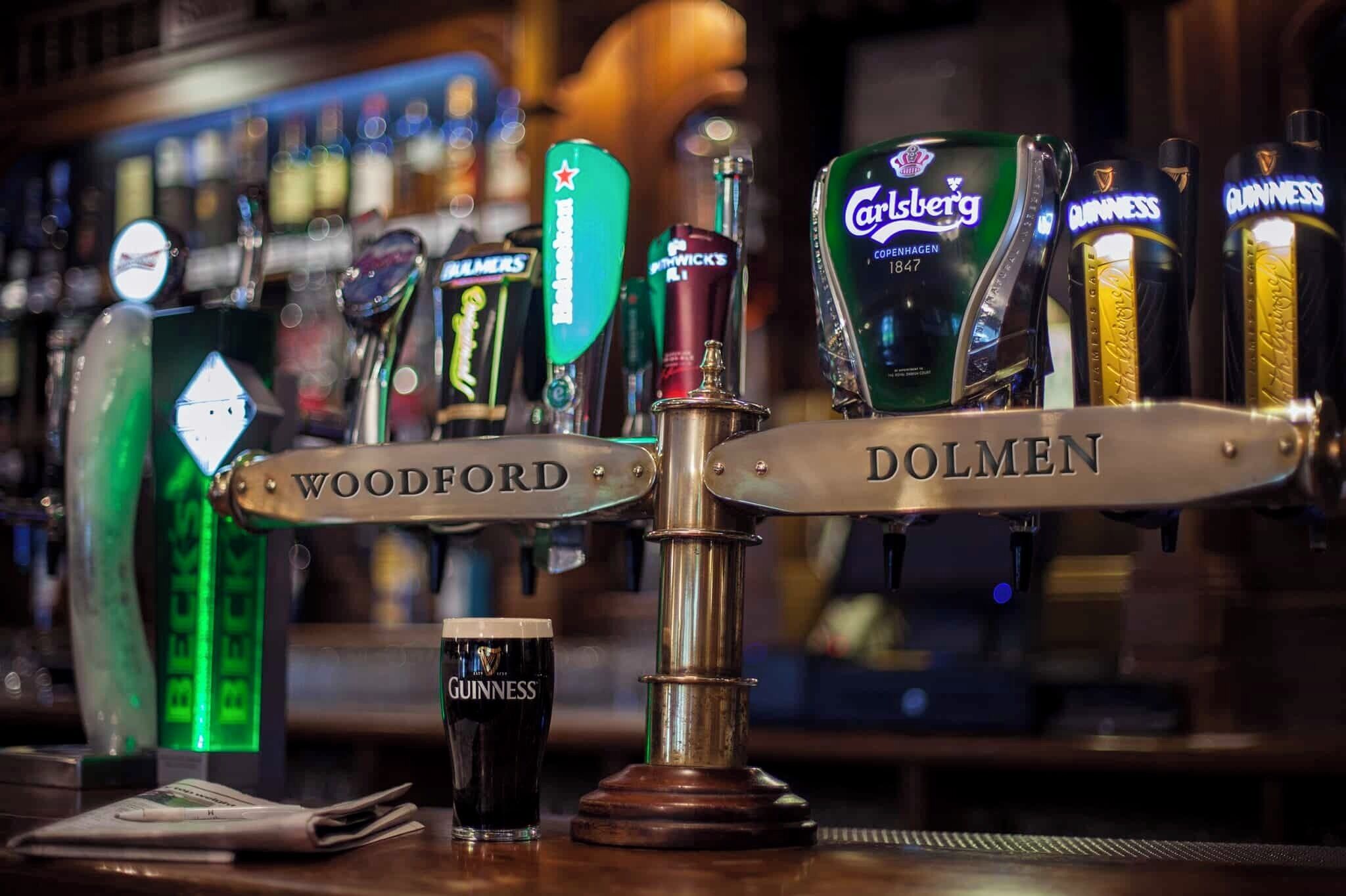 Um balcão de bar com várias torneiras de cerveja, incluindo marcas como Carlsberg, Guinness e Woodford.