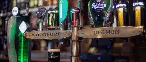 Um balcão de bar com várias torneiras de cerveja, incluindo marcas como Carlsberg, Guinness e Woodford.
