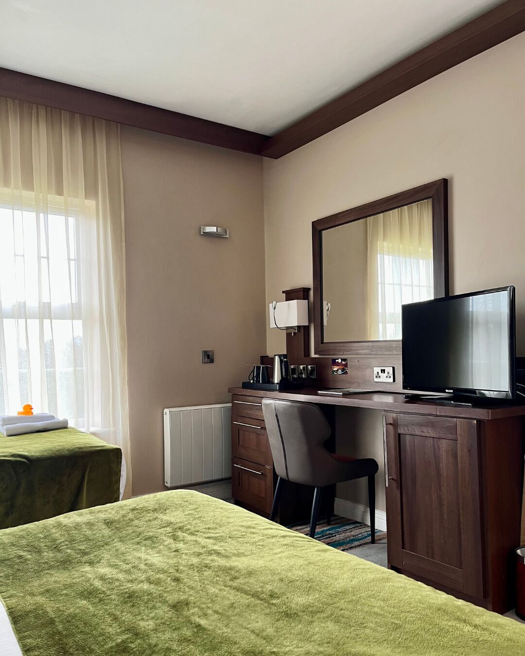 Une chambre d’hôtel avec deux lits, un bureau avec une chaise, une télévision et un grand miroir.