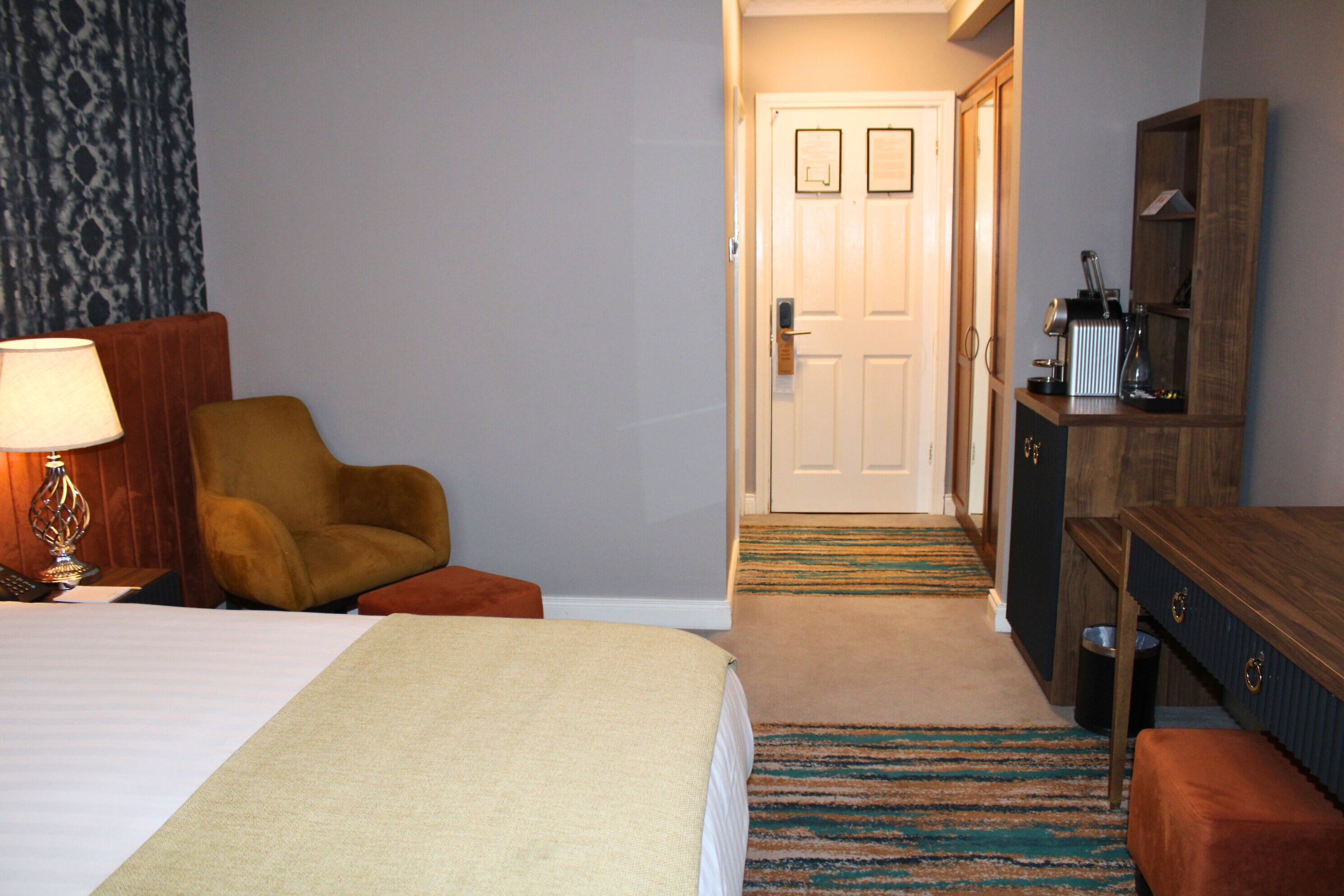A hotel room with a bed, a chair, a desk, and a lamp.