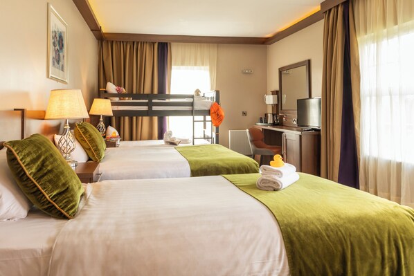 Habitación de hotel con dos camas, un escritorio, una silla, un televisor y una ventana con cortinas.