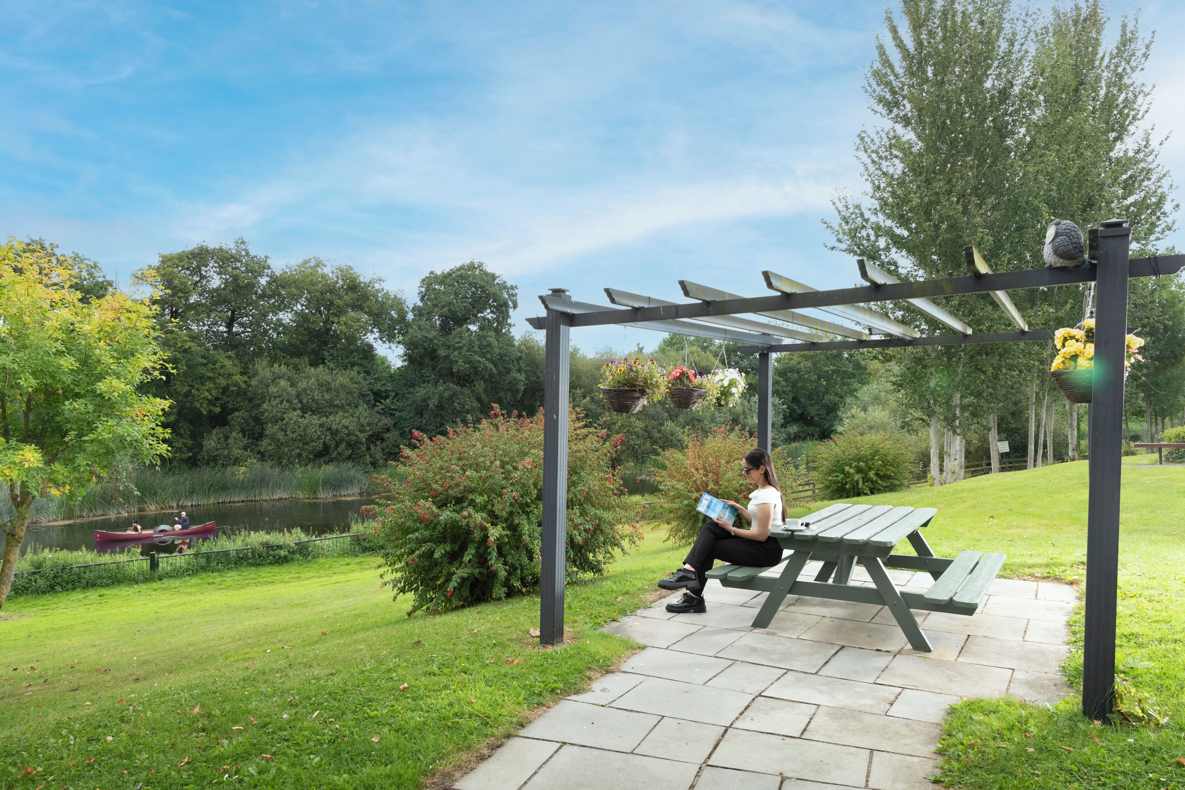 A covered picnic area with a bench, a table, and hanging flower baskets.