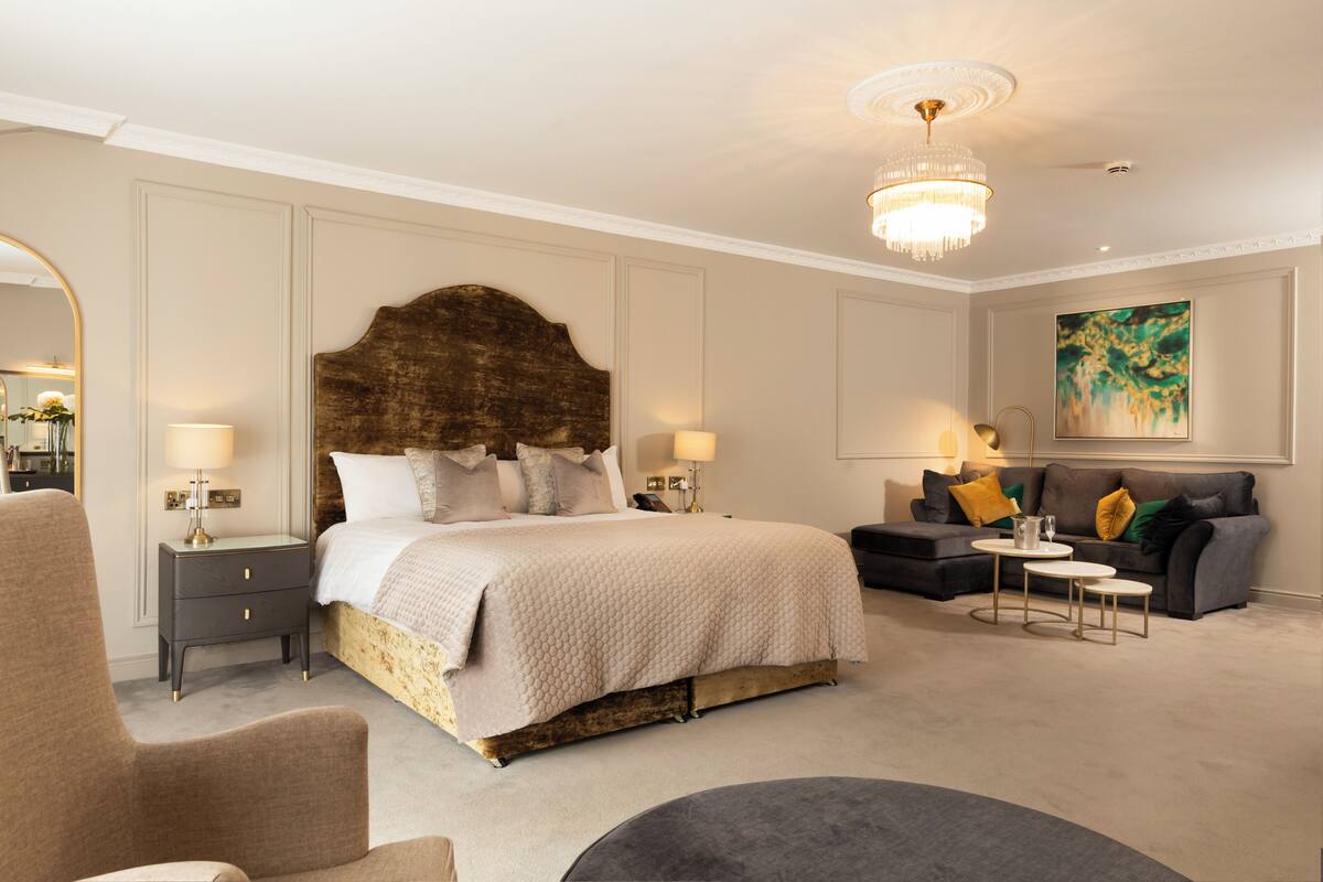 Ein Schlafzimmer mit einem großen Bett, Nachttischen, einem Sofa, einer Chandelieber und einem Gemälde.