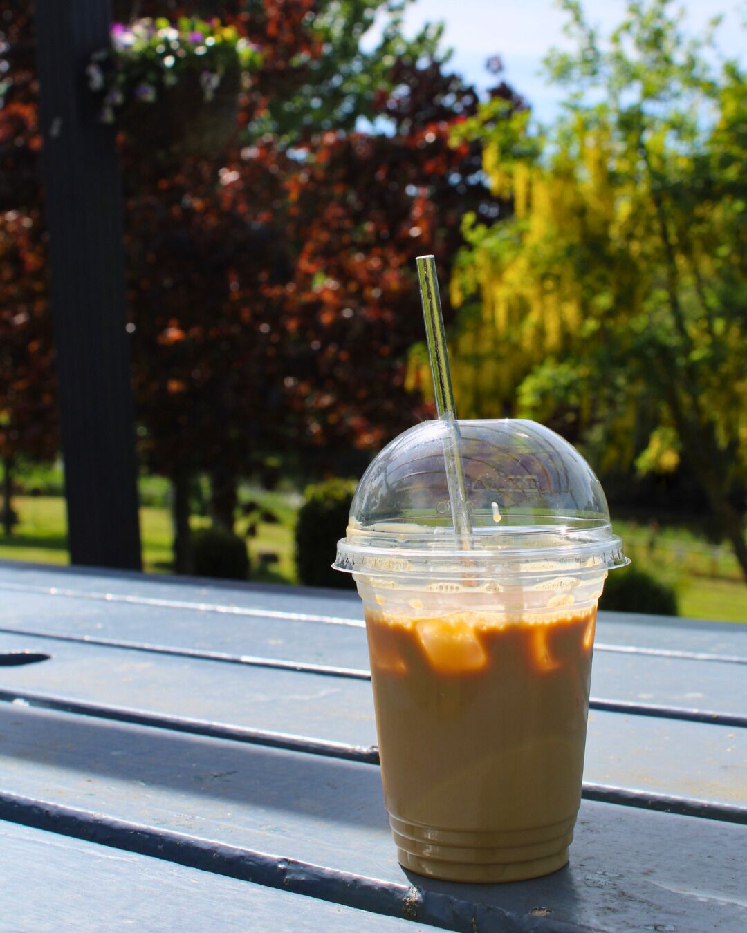 A clear plastic cup with a straw, containing a beverage, placed on a metal table outdoors.