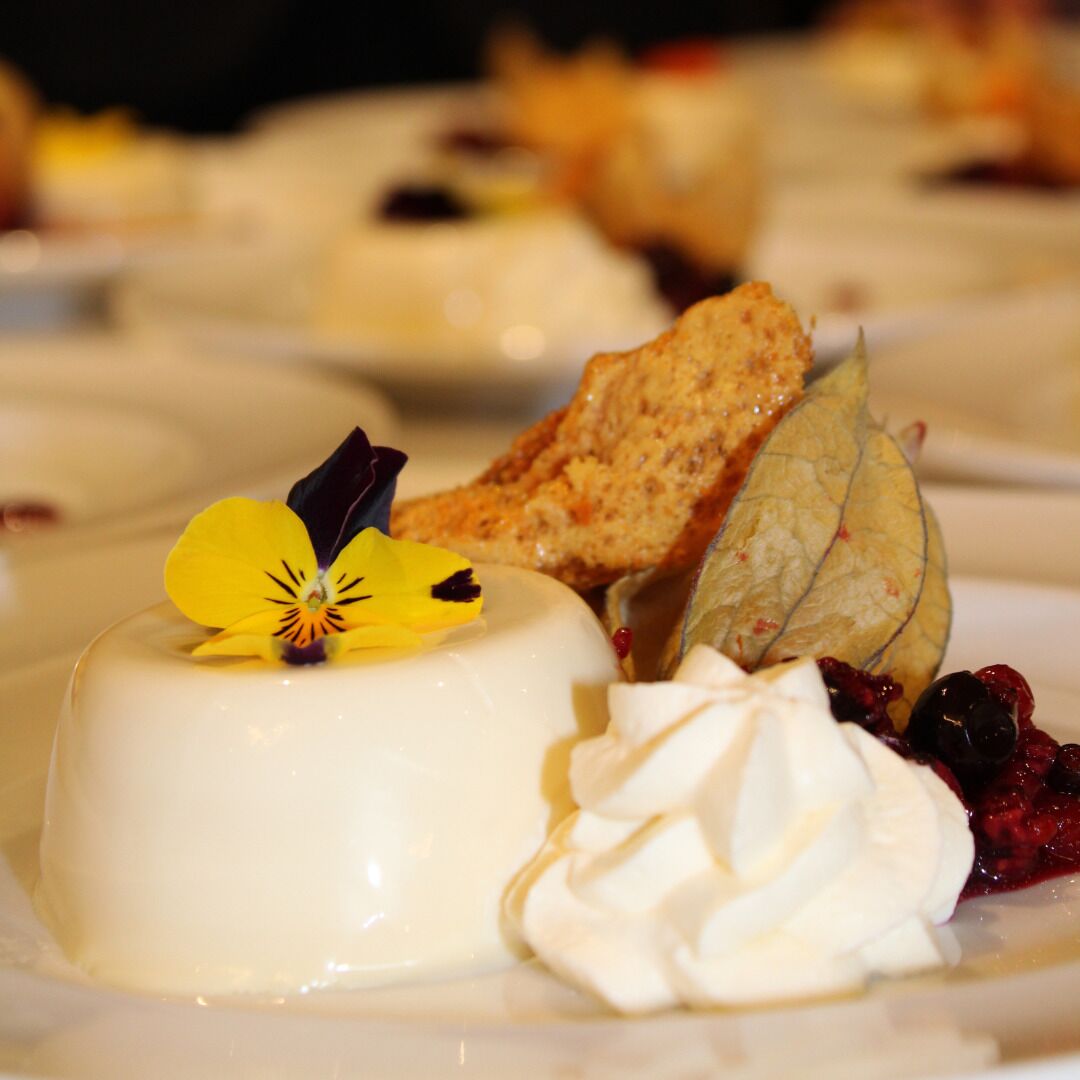 Un plato de postre con panna cotta blanca, una flor amarilla, crema batida y bayas.