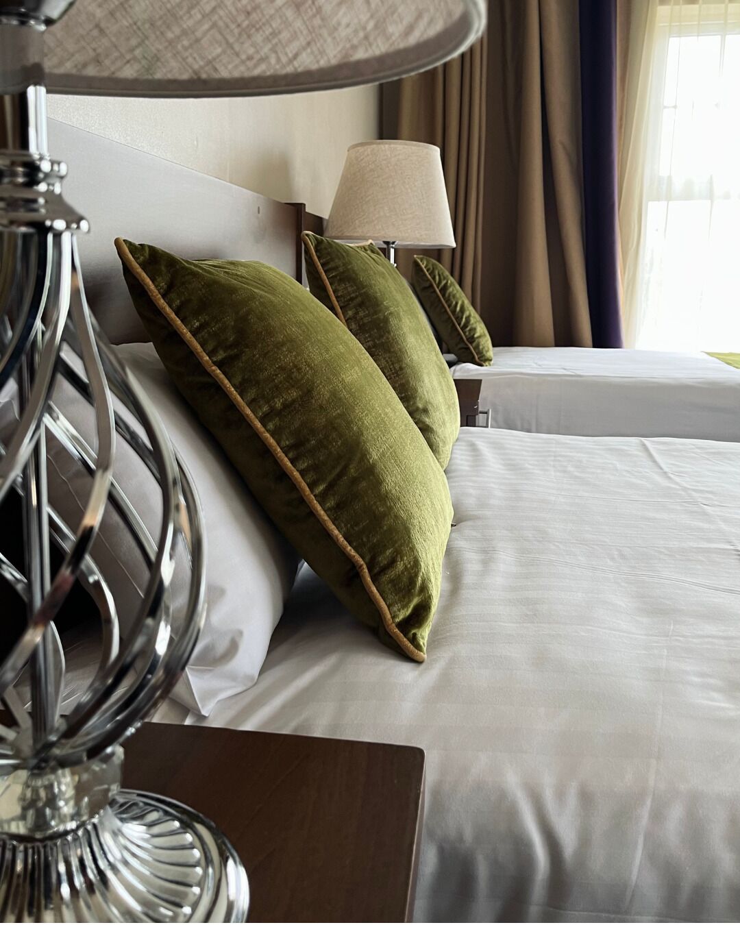 A hotel room with a bed, pillows, a lamp, and curtains.