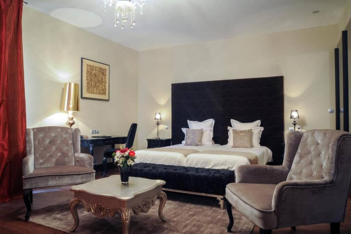 Une chambre d’hôtel avec un grand lit, deux tables de chevet, un bureau, une chaise, une table basse et un lustre.