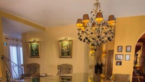 A grand piano in a spacious room with a chandelier, framed artwork on the walls, and a staircase leading to another area. - Demeure Loredana  (Saint-Florent)