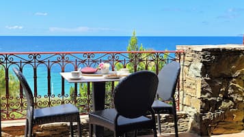 A balcony with two wicker chairs, a table with a white cup, pink flowers, and a plate of cookies.